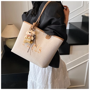 Detail of beige canvas tote with brown leather trim and cute plush bear accessory