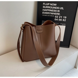 Détail d'un sac seau en cuir mat marron avec logo de la marque et large bandoulière