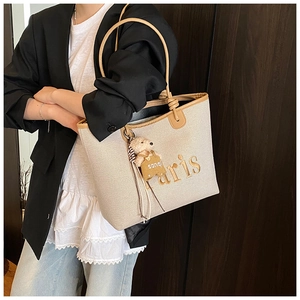Detail of beige canvas tote with brown leather trim and cute teddy bear charm