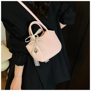 Detail of pink lychee leather handbag with lace bow, pearl charm and heart pendant