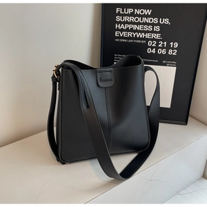 Détail d'un sac seau en cuir noir avec bandoulière réglable et logo gaufré sur marbre