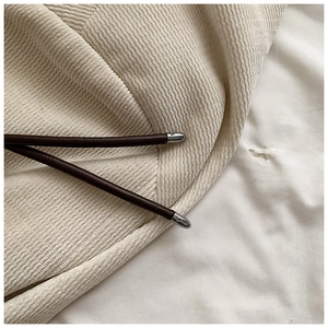 Close-up of beige corduroy fabric texture with brown leather drawstring and metal tips