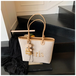 Detail of canvas tote bag with Paris embroidery and plush bear charm on dark steps
