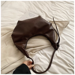 Detail of dark brown leather crescent bag with knot shoulder strap on soft fabrics