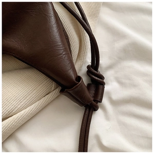 Macro detail of dark brown leather knot strap and smooth texture on the hobo shoulder bag