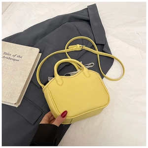Detail of yellow pebbled leather crossbody bag with white lace trim on grey suit background