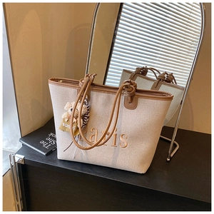 Detail of beige canvas bucket bag with Paris embroidery and teddy bear charm on black desk