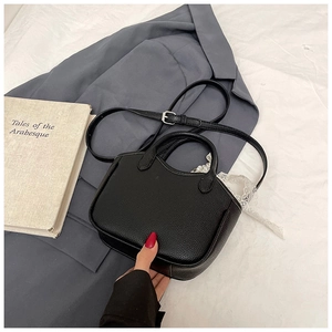 Detail of black litchi grain leather handbag with top handles on a vintage suit background