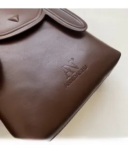 Close-up of the dark brown leather texture and embossed logo on the stylish crossbody bag