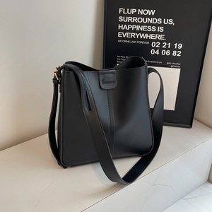 Sac seau chic en cuir noir avec large bandoulière sur surface en marbre pour femme