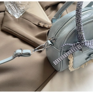 Detail of light blue crossbody bag with silver zipper and plaid ribbon bow decoration