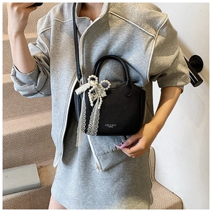 Elegant black lychee leather handbag with pearl bow and lace detail shown on shoulder