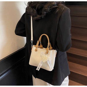 Detail of cream crossbody bucket bag with brown knotted handle and lace bow charm