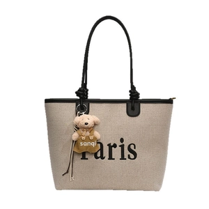 Off-white canvas tote bag with black trim, Paris logo, and a plush bear pendant