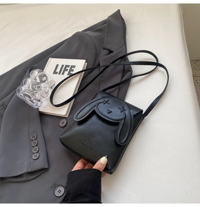 Detail of black crossbody bag with rabbit ear flap on a professional suit background