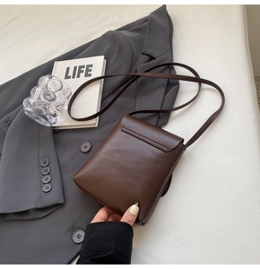 Vertical mini crossbody bag in dark chocolate faux leather placed on a grey blazer