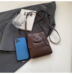 Detail of a dark brown rabbit face crossbody bag with embroidered eyes and brand logo