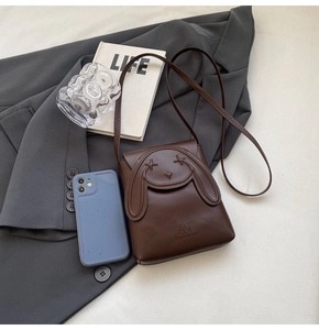 Detail of a brown leather mini crossbody bag with cute rabbit ears on an office desk