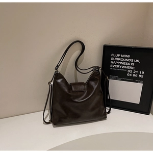 Détail d'un grand sac bandoulière en cuir café foncé avec texture lisse et fines lanières