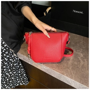 Detail of red bucket bag with litchi texture leather and elegant metal ball pendant