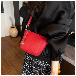 Detail of red litchi grain leather crossbody bag featuring heart-shaped tassel charm