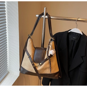 Détail du cabas en daim et cuir avec un pendentif baseball et des ferrures métalliques