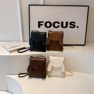 Cute bunny-ear mini crossbody bags in black, caramel, and beige on minimalist display