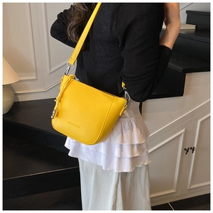 Detail of bright yellow bucket bag with lychee texture and woven knot charm on a shoulder strap