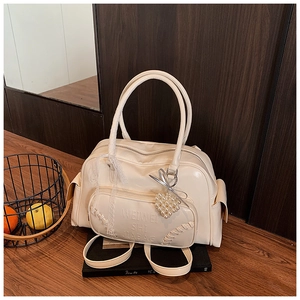 Dettaglio borsa in similpelle beige con ciondolo a cuore di perle e sciarpa in pizzo