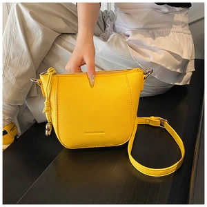 Detail of bright yellow crossbody bucket bag with litchi texture and metal hardware