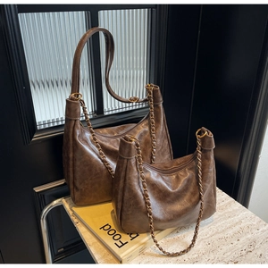 Set of two vintage brown leather tote bags with metal chains on marble surface