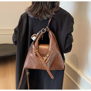 Détail du sac cabas en cuir marron foncé avec pendentif baseball sur blazer noir