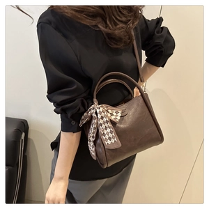 Dettaglio della borsa a secchiello in pelle marrone scuro con elegante foulard a scacchi
