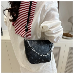 Détail d'un sac bandoulière noir avec chaîne argentée et motif ours sur chemise blanche