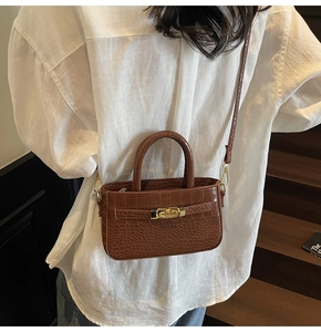 Close-up of brown crocodile texture handbag with gold rotating lock and top handles