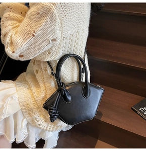 Detailed close-up of a black shell bag with knot decor shown in a lifestyle fashion setting
