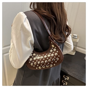 Brown leather crescent bag with silver stud rivets worn by a model in casual setting