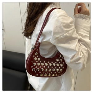 Detail view of burgundy leather shoulder bag with silver rivets worn by model