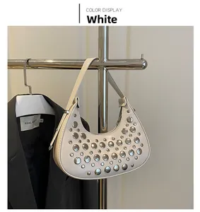 Detail view of white crescent bag with silver studs hanging on a metal rack
