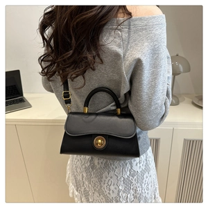 Schicke schwarze matte Umhängetasche mit goldenem Schloss am Modell in minimalistischer Umgebung