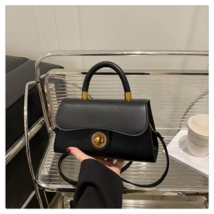 Detail der schwarzen matten Ledertasche mit goldenem Metalldrehverschluss und festem Griff