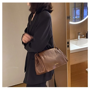 Brown leather tote bag with glossy finish and metal chain strap shown in a lifestyle setting