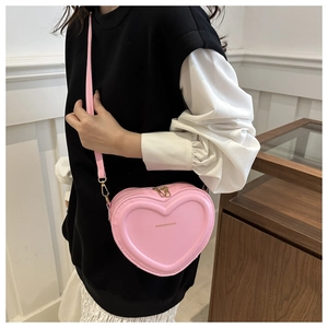 Detail of pink heart-shaped crossbody bag featuring gold lettering and metal zippers