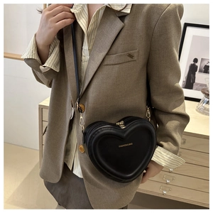 Detail of heart-shaped black PU leather bag with gold zipper worn by a model
