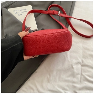 Close-up of bright red lychee grain leather texture and silver buckle on crossbody bag