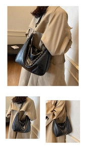 Detail view of black oiled leather tote bag with metallic chain on beige trench coat