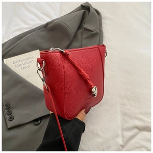 Detail of red pebbled leather bucket bag with silver metal pendant and knotted strap