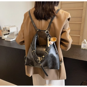 Détail du sac à dos en cuir noir avec ferrures dorées et breloque de baseball sur tenue