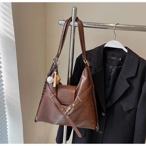 Détail du sac cabas en cuir marron avec boucle métallique et pendentif de baseball