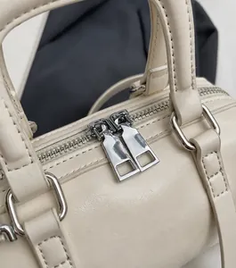 Detail of smooth silver dual zippers and fine leather texture on cream Boston bag